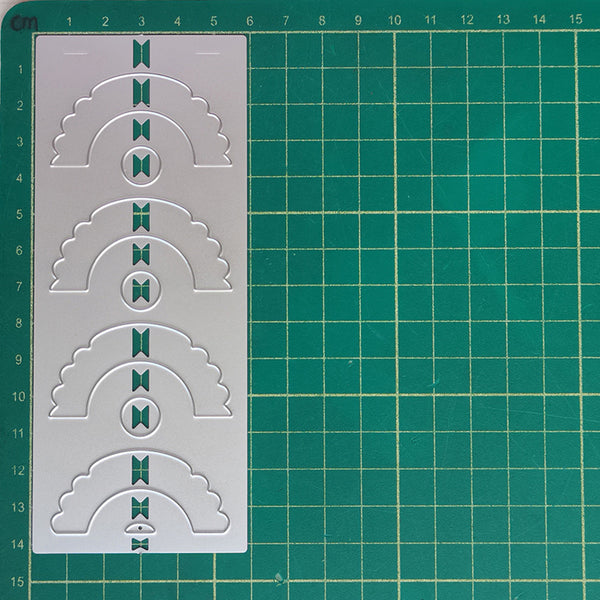 A white plastic stencil template featuring four arch and oval cutout patterns with bow details, displayed on a green cutting mat with grid lines.