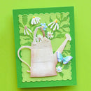 A handmade layered paper card featuring a 3D embossed watering can, white and blue daisies, green leaves, and a blue butterfly on a bright green background, set against a solid lime green backdrop.