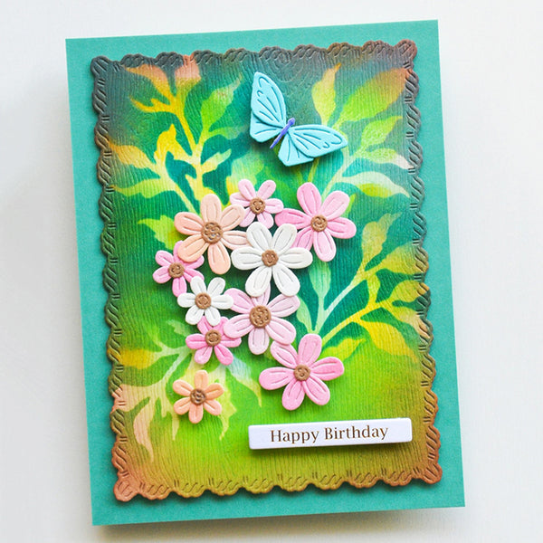 A handmade layered greeting card with a scalloped embossed border, featuring a green and yellow gradient background, pink and white daisy flowers, a light blue butterfly, and a white 'Happy Birthday' label at the bottom.
