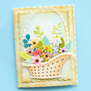 A handmade layered paper card featuring a woven basket filled with colorful paper flowers and green leaves, set against a pale blue background.