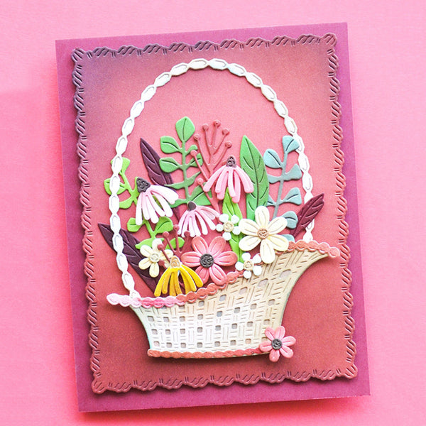 A handmade layered paper card featuring a 3D basket filled with colorful paper flowers and leaves, set against a pink background.
