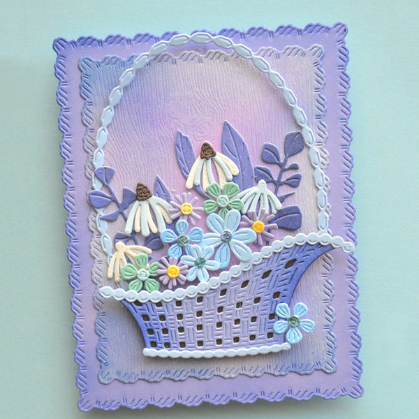 A handmade layered card featuring a lavender and purple basket filled with 3D die-cut flowers in shades of blue, green, white, and yellow, set against a light mint green background.