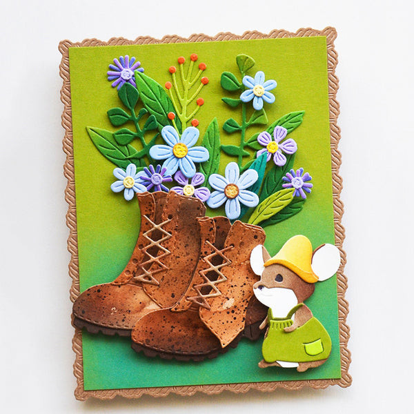 A handmade paper craft card featuring a pair of brown lace-up boots, a small mouse in green clothing and a yellow hat, and blue and purple flowers with green leaves on a green background.