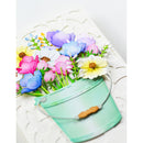A decorative artificial flower arrangement in a small mint green bucket with a metal handle and wooden accent, photographed on a white textured background.