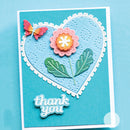 A handmade layered card featuring a large textured light blue heart with a white scalloped border, a pink flower with green leaves, a small pink butterfly, and a die-cut 'thank you' script at the bottom, set against a solid blue background.