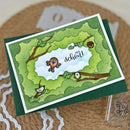 A handmade greeting card featuring a forest-themed design with birds, branches, and the words 'and school!', shown resting on a dark green envelope over a woven surface.