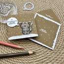 A handmade greeting card set featuring a cute gray cartoon cat on a brown background with white snow dots and a speech bubble reading 'EIN Engelchen hat mir verraten.