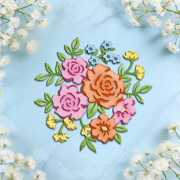 A flat-lay of a colorful floral arrangement made from layered paper or felt flowers and leaves, centered on a light blue marble surface with white baby's breath flowers framing the edges.