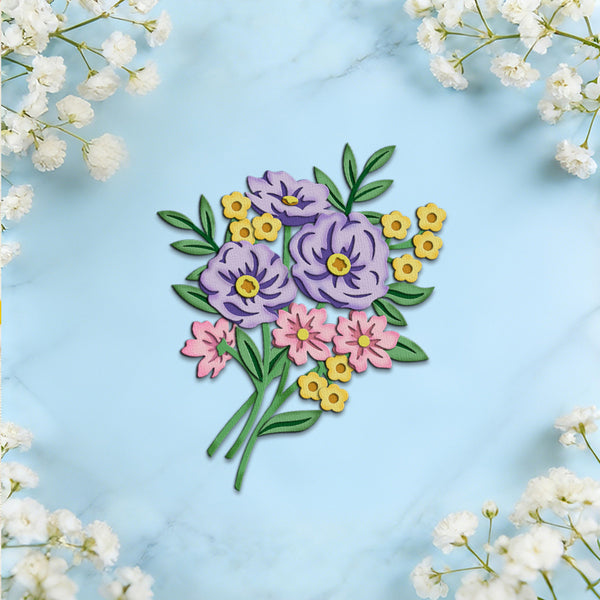 A colorful floral applique or embroidered patch featuring purple, pink, and yellow flowers with green leaves, arranged on a light blue marble background with white baby's breath flowers framing the corners.