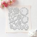 A flat lay of a metal die-cutting or stamping template sheet with multiple floral and decorative cutout shapes, placed on a white surface with pink flowers in the top left and a small white ceramic object in the bottom right.