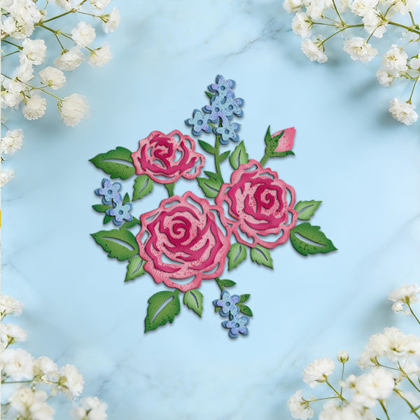 An embroidered floral design featuring two pink roses with green leaves and small blue flowers, arranged on a light blue marble background with white baby's breath flowers framing the edges.