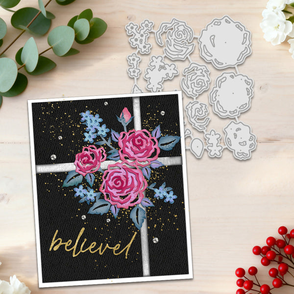 A handmade greeting card with a floral window design and the word 'believe' in gold script, shown next to matching metal die-cutting templates on a light wood surface with decorative greenery and berries.