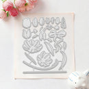 A floral die-cut craft template or stencil sheet with multiple flower, leaf, and ribbon outlines, photographed on a white surface with pink flowers and a small white decorative object as props.