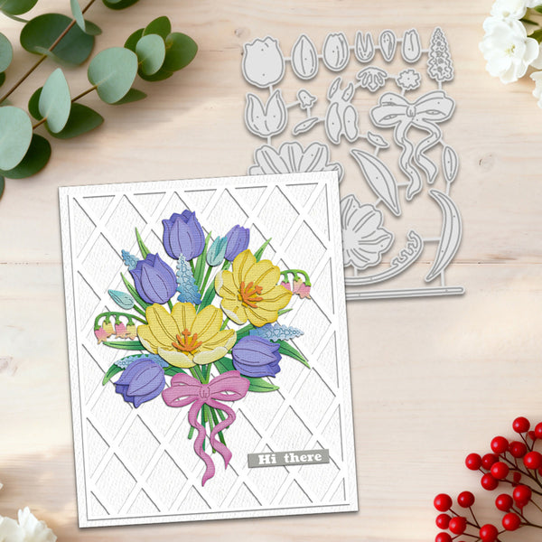 A handmade greeting card with a colorful tulip bouquet and the words 'Hi there' on the front, displayed next to a silver floral die-cut metal cutting template on a light wood background with decorative eucalyptus and red berries.