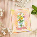 A handmade greeting card with a floral illustration and the words 'Have a lovely day' on a pink gingham background, styled on a light wood surface with white flowers and mint leaves.