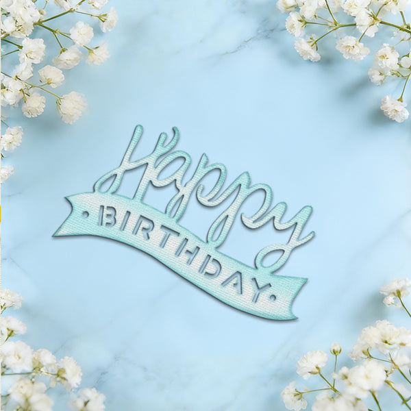 A light blue and white 'Happy Birthday' script cake topper placed on a light blue marble background, framed by white baby's breath flowers in the corners.