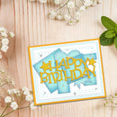 A handmade square birthday card with layered light blue and yellow shapes and the words “HAPPY BIRTHDAY” in yellow, styled on a light wood surface with white flowers and mint leaves around it.
