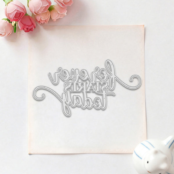 A silver metal die-cut lettering template featuring the phrase 'I love you silently' in elegant cursive, displayed on a square sheet of white cardstock. The setup is styled as a flat-lay with pink roses in the top-left corner and a small white ceramic pig in the bottom-right corner, all on a clean white background.