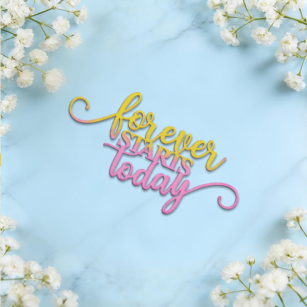 A decorative script sign reading 'forever starts today' in yellow, pink, and orange gradient lettering, placed on a light blue marble surface with white flowers framing the corners.