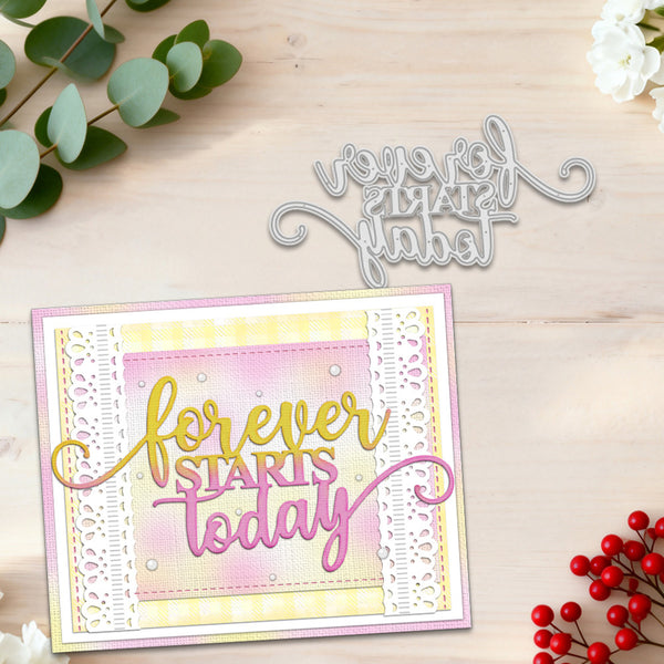 A handmade greeting card with layered pastel pink, yellow, and white borders, featuring the phrase 'forever STARTS today' in gold and pink script, shown on a light wood surface with a matching metal die cutter above it. Decorative eucalyptus leaves and red berries frame the scene.