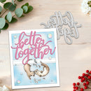 A handmade greeting card with a die-cut design featuring two otters and the phrase 'better together' in pink script, shown on a light wood surface with a matching metal die and decorative greenery and red berries.