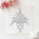 A flat rectangular sheet with a metallic geometric floral or leaf-like cutout design, photographed on a light background with pink flowers in the top left and a small white decorative object in the bottom right.
