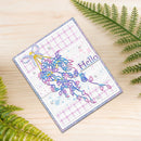 A handmade greeting card with a colorful abstract tree design, a lavender plaid pattern, and the word 'Hello' on a wooden surface, styled with green fern leaves.