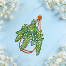 An orange and green hanging planter die-cut sticker or decal featuring a fern design, displayed on a light blue marble background with white baby's breath flowers in the corners.