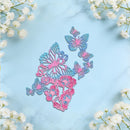 A decorative paper cutout featuring butterflies and floral motifs in pink and blue, arranged on a light blue marble surface with white baby's breath flowers framing the edges.
