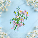 A decorative floral arrangement featuring pink and white daisies with green stems and leaves, tied with a pink ribbon, displayed on a light blue marble surface surrounded by white baby's breath flowers.