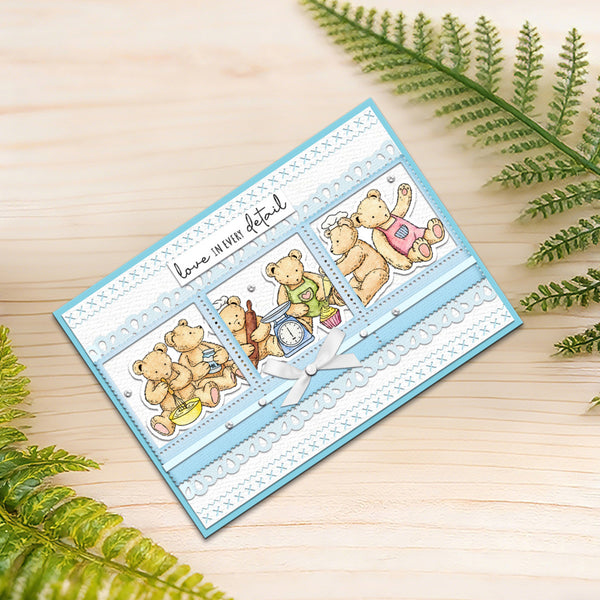 A handmade baby shower card featuring three teddy bear illustrations in different outfits, set on a light wood background with green fern leaves. The card is light blue and white with a small white bow.