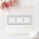 A rectangular metal die with three scalloped border frames and empty center panels, placed on a light pink sheet over a white background with pink flowers and a small white ceramic object in the corners.