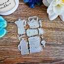 A set of six silver metal coffee-themed dies arranged on a rustic wooden surface, surrounded by decorative flowers and a partial candle jar.