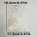 A laser-cut metal floral corner embellishment with lily-of-the-valley and bird motifs, shown on a textured light background with dimension labels of 16.2cm by 11.