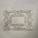 An ornate rectangular metal frame with intricate scrollwork and cutout details, displayed against a textured light beige background.