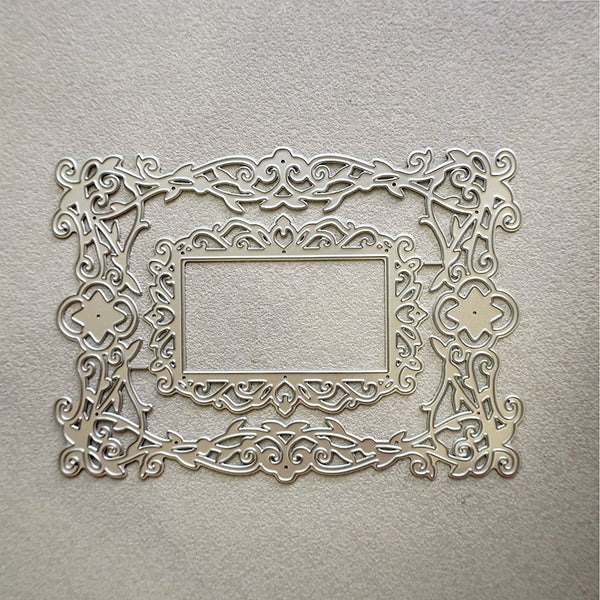 An ornate rectangular metal frame with intricate scrollwork and cutout details, displayed against a textured light beige background.