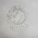 A white laser-cut metal ornament featuring a bird perched on a flowering branch inside an oval frame, with decorative scrollwork and the phrase 'To those who love and are loved' cut along the bottom, displayed on a textured white background.