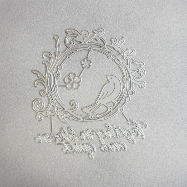 A white laser-cut metal ornament featuring a bird perched on a flowering branch inside an oval frame, with decorative scrollwork and the phrase 'To those who love and are loved' cut along the bottom, displayed on a textured white background.