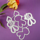 Four silver metal die-cut craft shapes, including a butterfly, a bear, a bee, and a cat, arranged on a purple background with a yellow and orange flower in the top left corner.