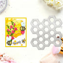 A handmade greeting card with a yellow honeycomb and bee design is shown next to a metal die-cutting template featuring matching honeycomb shapes, styled on a white surface with flowers and makeup brushes.