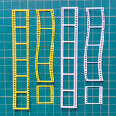 Four plastic film sprocket-edge molds in yellow and white, laid out on a green cutting mat with a grid.
