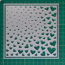 A square metal craft stencil with a pattern of small and large heart cutouts, displayed on a green cutting mat.