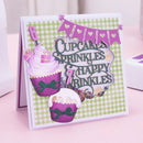 A handmade 7th birthday card featuring two decorated cupcakes, a purple banner with hearts, and the text 'Cupcakes Sprinkles Happy 7th Birthday' on a green and white checkered background, displayed on a pink surface.