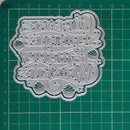 A silver metal cutting die with a decorative 'Happy Cupcakes, Pankakes, Weekakes' design, displayed on a green cutting mat with grid lines.