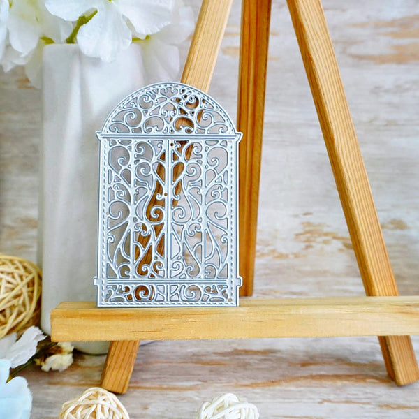 A decorative silver metal arch ornament with intricate filigree cutouts, displayed on a wooden easel stand.