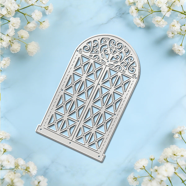 An arched metal die-cut template with an intricate geometric and scrollwork pattern, displayed on a light blue marble background with white baby's breath flowers in the corners.