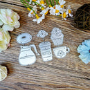 A set of five coffee-themed metal cutters, including a coffee pot, coffee cup, cupcake, donut, and coffee bean sprout, arranged on a rustic wooden surface with decorative flowers.