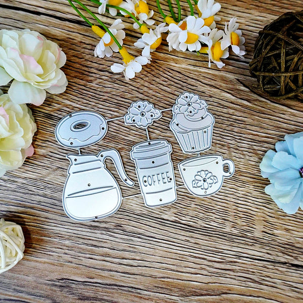 A set of five coffee-themed metal cutters, including a coffee pot, coffee cup, cupcake, donut, and coffee bean sprout, arranged on a rustic wooden surface with decorative flowers.