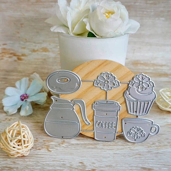 A set of metal cookie cutters shaped like a coffee mug, coffee cup, donut, cupcake, and teacup, displayed on a wooden board with a white flower pot in the background.