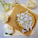 A floral metal cutout with butterflies and layered circular wire designs, displayed on a burlap square over cream paper with decorative white flowers and a woven ball prop.